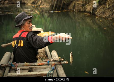 Un ranger del parco nazionale che indossa una giacca Brimob (Indonesian Mobile Brigade Corps) sta pescando dalla barca sul fiume Cigenter, mentre sta facendo una pausa dal viaggiare attraverso la foresta costiera dell'Isola di Handeuleum nel Parco Nazionale di Ujung Kulon, Pandeglang, Banten, Indonesia. Foto Stock