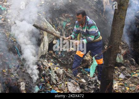 Un uomo che brucia spazzatura in un sito di scarico illegale nella città di Kashmirs Sopore Foto Stock