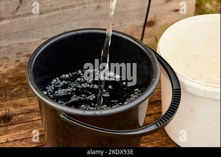 un secchio di plastica nera è riempito di acqua dalla pompa Foto Stock