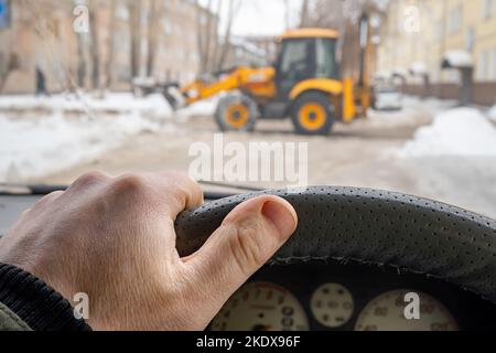 mano del conducente sul volante contro lo sfondo di un trattore davanti alla vettura Foto Stock