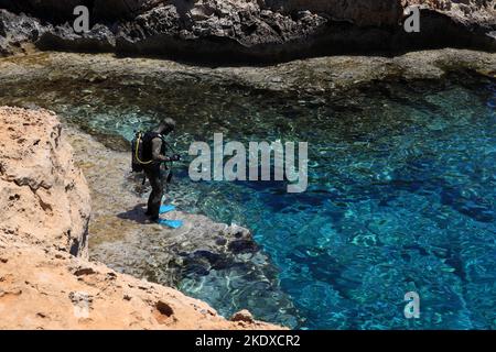 29 maggio 2022, Larnaca, Cipro: Un subacqueo si prepara a tuffarsi nella laguna blu del Mar Mediterraneo presso il Parco Nazionale della Foresta di Capo Greco, all'estremità meridionale della Baia di Famagosta, e fa parte del comune di Ayia Napa. La Repubblica di Cipro si trova a un crocevia storico-culturale tra Europa e Asia. Le sue principali città, la capitale di Nicosia, Limassol, Famagosta e Paphos, hanno assorbito le influenze di generazioni di conquistatori, pellegrini e viaggiatori e hanno un'aria cosmopolita e provinciale. Oggi Cipro è una destinazione turistica popolare per i visitatori provenienti dall'Europa, Foto Stock