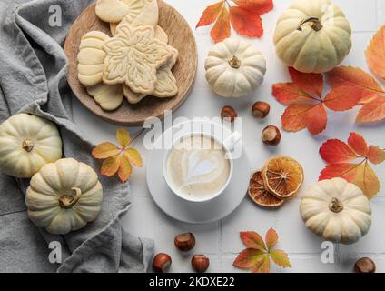 Accogliente composizione autunnale. Caffè caldo con biscotti in una tazza bianca circondata da foglie autunnali e zucche su uno sfondo di legno bianco. Foto Stock