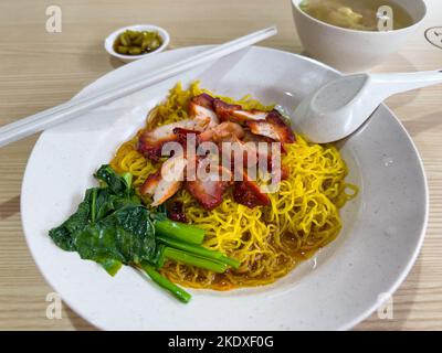 Spaghetti all'uovo secchi, maiale alla griglia in stile cantonese, zuppa di brodo caldo con wanton, peperoncino a fette verdi, un pasto decente al Hawker Center di Singapore Foto Stock