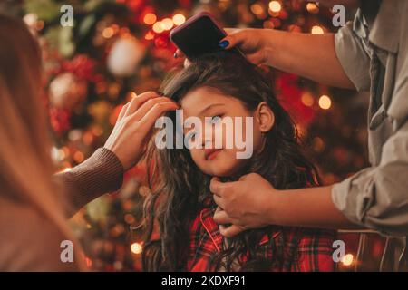 Felice giappone piccola ragazza sognatore guardando via miracolo di attesa da Santa posa vicino a noel albero. Capelli ricci neri asiatici capretto in abito rosso celebrato a plaid Foto Stock