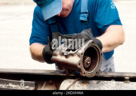 Il meccanico di riparazione dell'automobile ispeziona attentamente la parte. Riparazione meccanica del motore. Flusso di lavoro. Vista frontale. Foto Stock