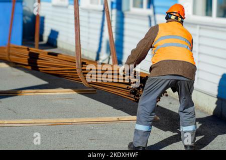 Slinger raccoglie tubi metallici sottili in pila in cantiere. Primo piano. Flusso di lavoro reale. Scarico di materiali per costruzione. Background di produzione per il fornitore di attrezzature.. Foto Stock