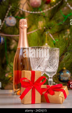 Scatole regalo e bicchieri di cristallo sfocati, bottiglia di champagne e albero di Natale con luci scintillanti e palle giocattolo. Foto Stock