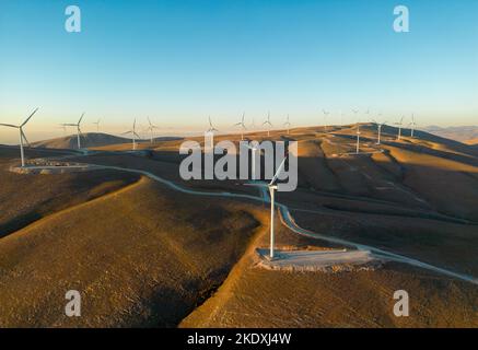 Vista aerea di più turbine eoliche in piedi su una collina e che generano elettricità all'alba Foto Stock