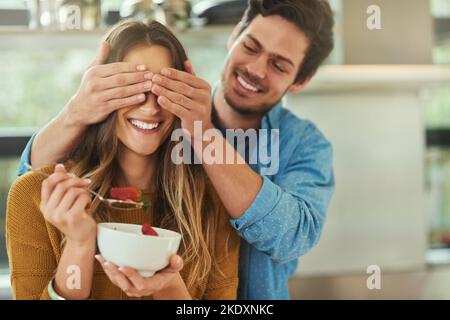 Mi chiedo chi potrebbe essere... un giovane affettuoso che copre gli occhi delle sue amiche mentre mangia la colazione in cucina. Foto Stock