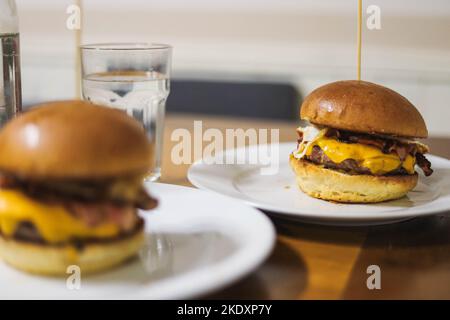 Delizioso hamburger con stuzzicadenti mentre servito su un piatto bianco posto sul tavolo Foto Stock