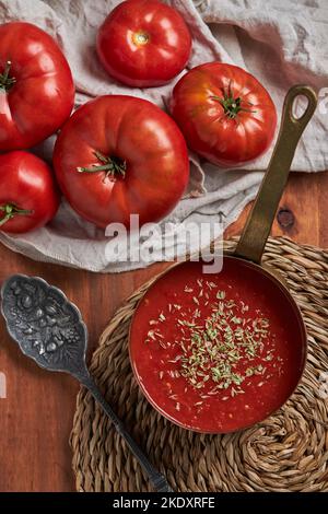 Vista dall'alto della padella con deliziosa salsa di pomodoro fatta in casa e cospargere di origano posto su un tappeto intrecciato su un tavolo di legno in cucina Foto Stock