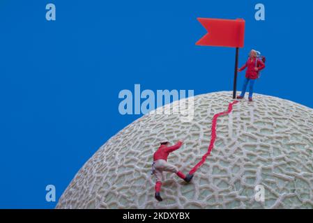 Giocattoli in miniatura - un gruppo di alpinisti che raggiungono la cima. Rock melone frutta come base. Foto Stock