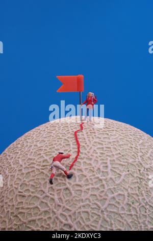 Giocattoli in miniatura - un gruppo di alpinisti che raggiungono la cima. Rock melone frutta come base. Foto Stock