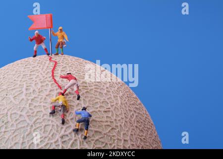 Giocattoli in miniatura - un gruppo di alpinisti che raggiungono la cima. Rock melone frutta come base. Foto Stock