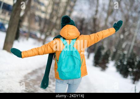 Retro dietro la vista di una bambina che indossa un caldo vestito e che si diverte a passeggiare in inverno con il tempo innevato all'aperto Foto Stock