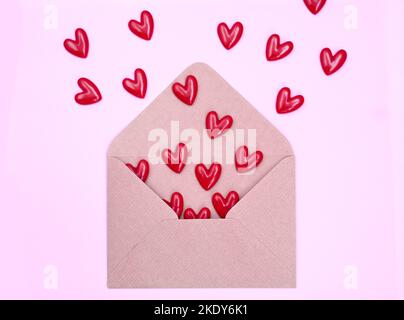 Busta e cuori rossi su sfondo rosa. San Valentino, amore, concetto di anniversario Foto Stock