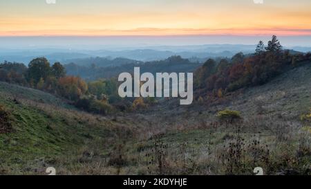 Paesaggio rurale durante il crepuscolo in autunno, campagna collinare con lussureggianti foreste colorate e arancione bagliore nel cielo Foto Stock
