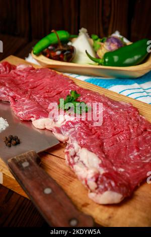 Un maiale crudo con verdure e spezie su tavola di legno, colpo verticale Foto Stock