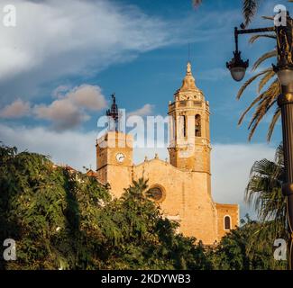 Un angolo basso di una chiesa cattolica vicino al giardino, sotto un cielo blu durante il giorno a Sitges, Spagna Foto Stock