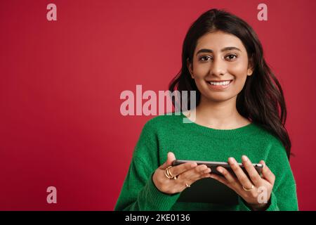 Giovane donna indiana sorridente e che utilizza un computer tablet isolato su sfondo rosso Foto Stock