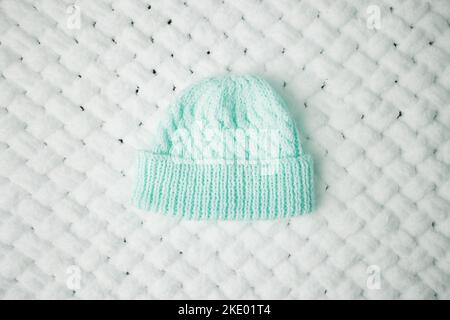 Un piccolo cappello caldo lavorato a maglia su una morbida coperta bianca Foto Stock