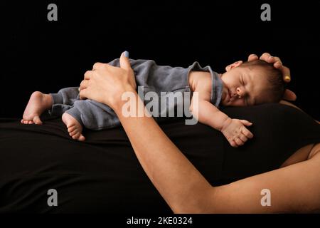 Giovane madre sdraiata tenendo il bambino su uno sfondo scuro Foto Stock