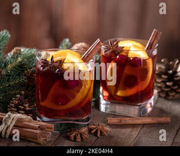VIN brulé con fettine d'arancia, mirtilli rossi e spezie su un rustico tavolo di legno e sfondo Foto Stock