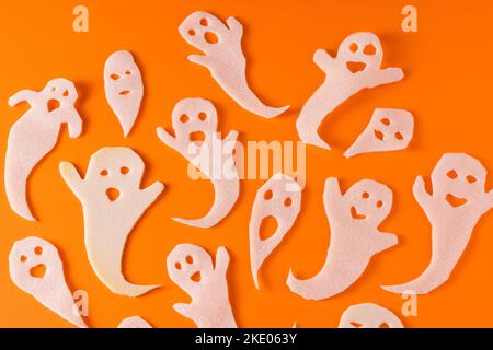 Fantasmi bianchi bambini di mestiere per Halloween. Immagine fantasma della carta di avvolgimento su sfondo arancione vista dall'alto. Un mostro pauroso e divertente giocattolo con le tue mani. Fumetto Creepy Whisper. Fai-da-te fatto a mano. Impostare i caratteri boo Foto Stock