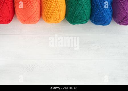 Molte palle multicolore di fili su tessuto lavorato a maglia su sfondi di legno bianco. Filati di fiori colorati, di maglieria e di crostini. Ago Foto Stock