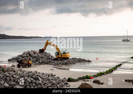 I lavoratori edili che utilizzano macchinari pesanti per impianti per spostare la pietra da cava in posizione per riparare le difese marine dopo che l'erosione costiera ha danneggiato il muro marino Foto Stock