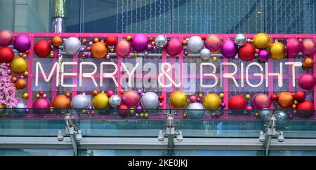 L'insegna esterna dice Merry & Bright con decorazioni natalizie o natalizie nel centro commerciale Arndale nel centro di Manchester, Regno Unito Foto Stock