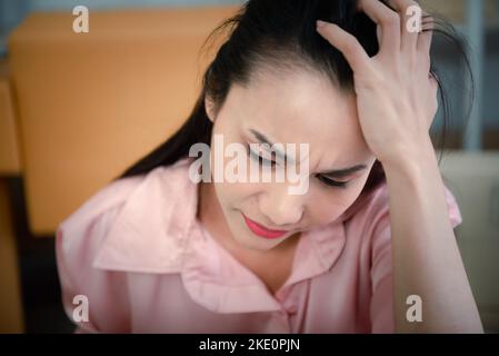 Giovane donna asiatica che soffre di mal di testa sul posto di lavoro. Foto Stock