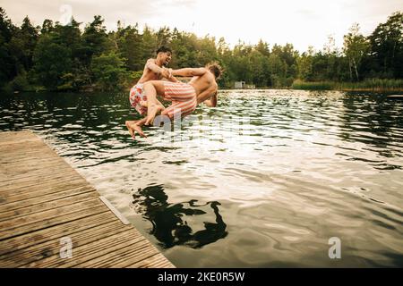 Amici maschi giocosi che saltano insieme in lago durante le vacanze Foto Stock