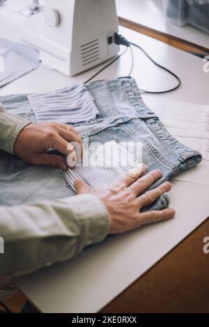 Mani del designer di moda che regola la tasca posteriore sui jeans in officina Foto Stock