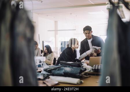 Stilisti di moda che tengono pacchetti mentre lavorano insieme in officina Foto Stock
