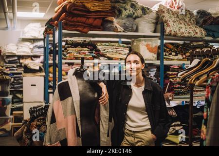 Ritratto di stilista femminile con mano in tasca appoggiata al manichino in officina Foto Stock