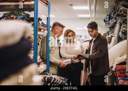 I designer di moda multirazziale discutono mentre tengono il tessuto in officina Foto Stock