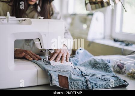 Sezione intermedia del tessuto professionale di cucitura di design femminile attraverso la macchina da cucire in officina Foto Stock