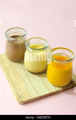Caramello, cioccolato e budino di mango in un vaso di vetro su sfondo rosa Foto Stock