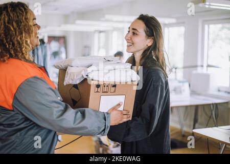 Buon stilista di moda che riceve il pacchetto da una persona di consegna femminile in officina Foto Stock