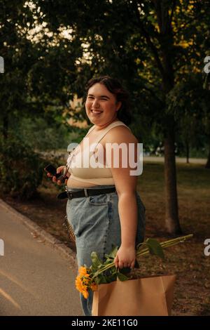 Ritratto di donna felice con girasole e shopping bag in piedi sulla strada Foto Stock