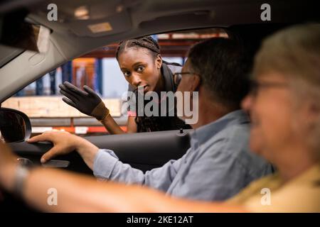 Il personale addetto alle vendite guida i clienti seduti in auto presso il negozio di hardware Foto Stock