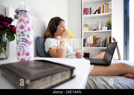 Vista laterale di una bella donna che gioca sul notebook, sdraiata sul letto Foto Stock