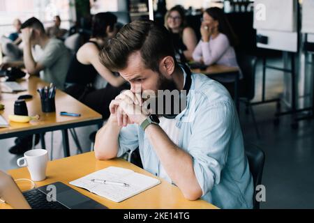 Un uomo d'affari preoccupato che lavora sul computer portatile alla scrivania sul posto di lavoro Foto Stock