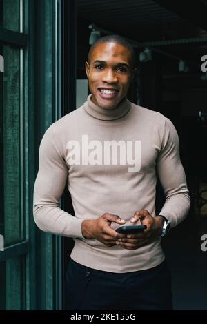 Ritratto di un uomo d'affari sorridente con smartphone alla porta d'ufficio Foto Stock