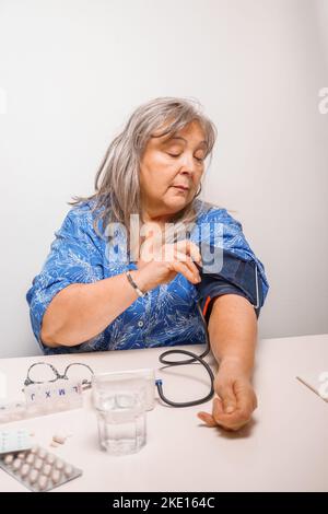 donna anziana dai capelli bianchi che prende la sua pressione sanguigna a casa Foto Stock