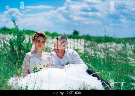 La sposa e lo sposo sono seduti in un campo Foto Stock