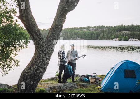 Uomo maturo che parla con un amico in piedi sul lago durante il campeggio Foto Stock