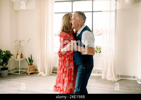 Vista laterale di un uomo anziano sorridente che tiene la mano di una donna mentre ballava in classe Foto Stock