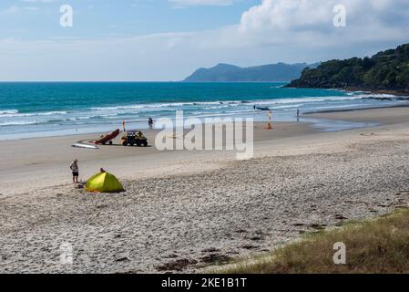 Alcune persone che praticano surf, pesca, campeggio e bagnini pattugliano sulla spiaggia di Waipu Cove a Northland, in Nuova Zelanda, in autunno, durante la giornata di sole Foto Stock